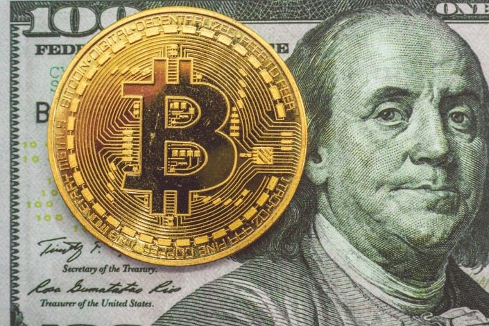 Round gold Bitcoin placed on a $100 bill